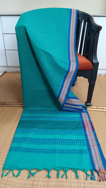 Refreshing turquoise cotton saree featuring a contrasting deep blue border and subtle geometric block prints in a darker turquoise shade. Perfect for adding a cool and calming touch to your everyday look.