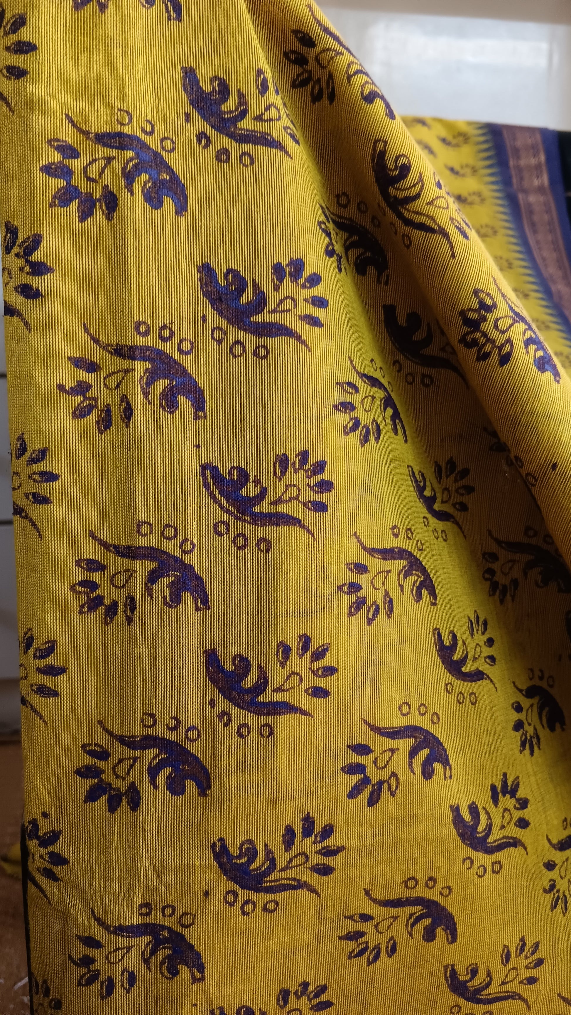 Close up view of the floral pattern block printed on the body of a yeloow function wear cotton saree with blue border