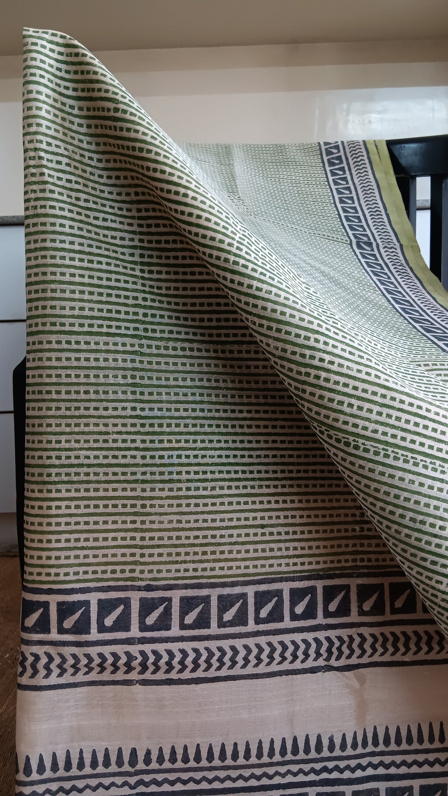 Close up view of the geometric pattern hand block printed on the body of a simple green daily wear silk cotton saree