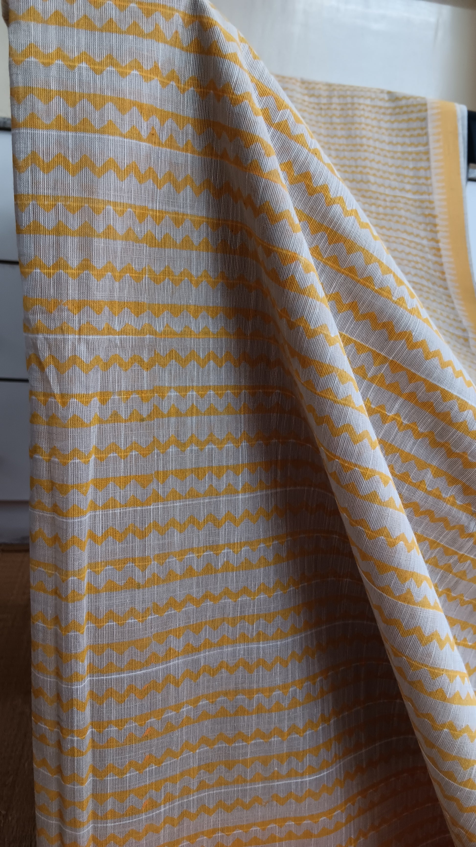 close up view of the geometric patterns block printed in mustard on the grey body of a daily wear cotton saree