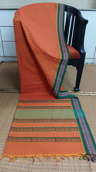 Bold rust cotton saree featuring striking green zari border and eye-catching chevron block prints. Perfect for making a confident statement at work or for daily wear.