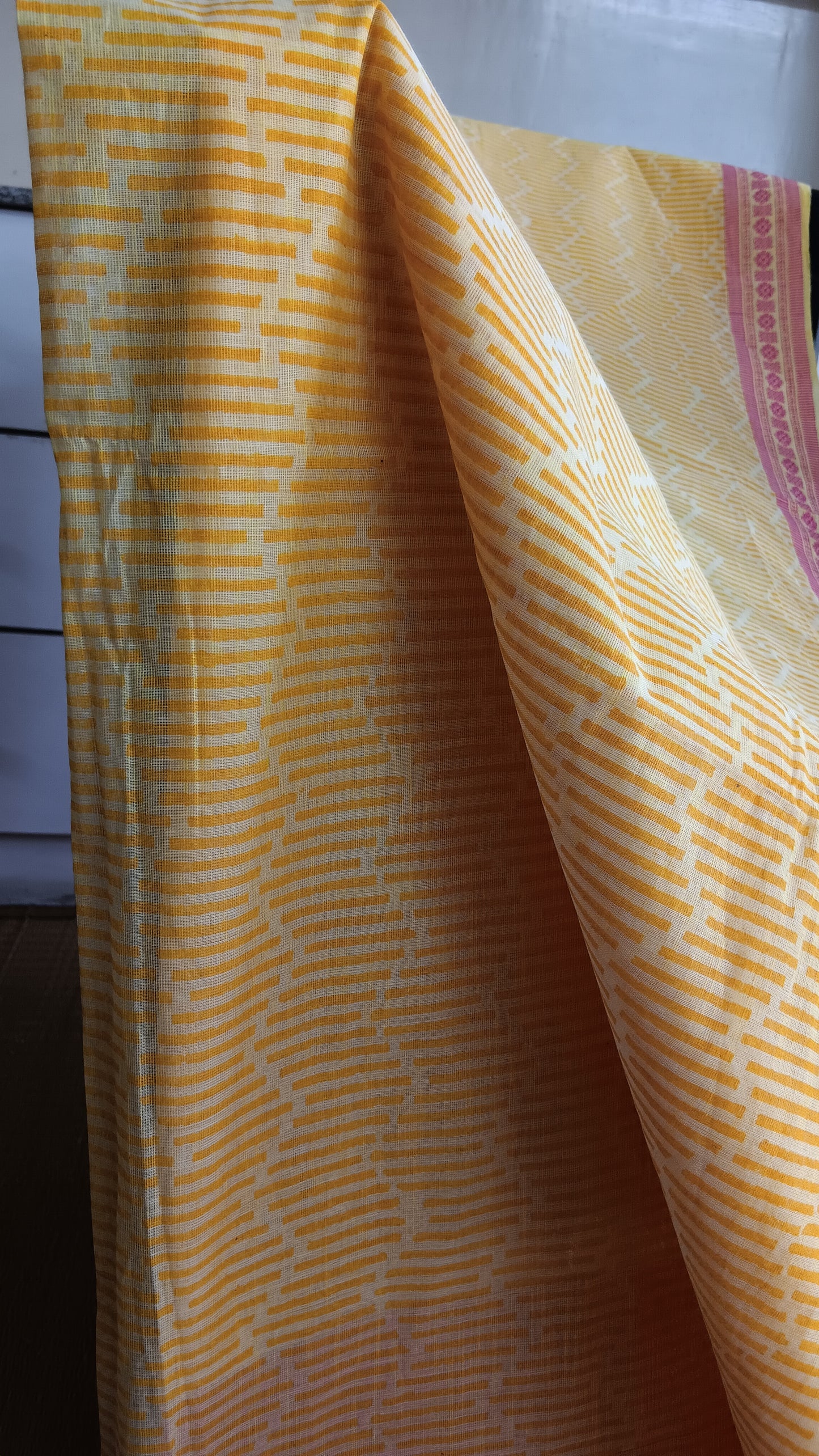 close up view of the bold geometric pattern block printed on the body of a yellow cotton saree with pink border